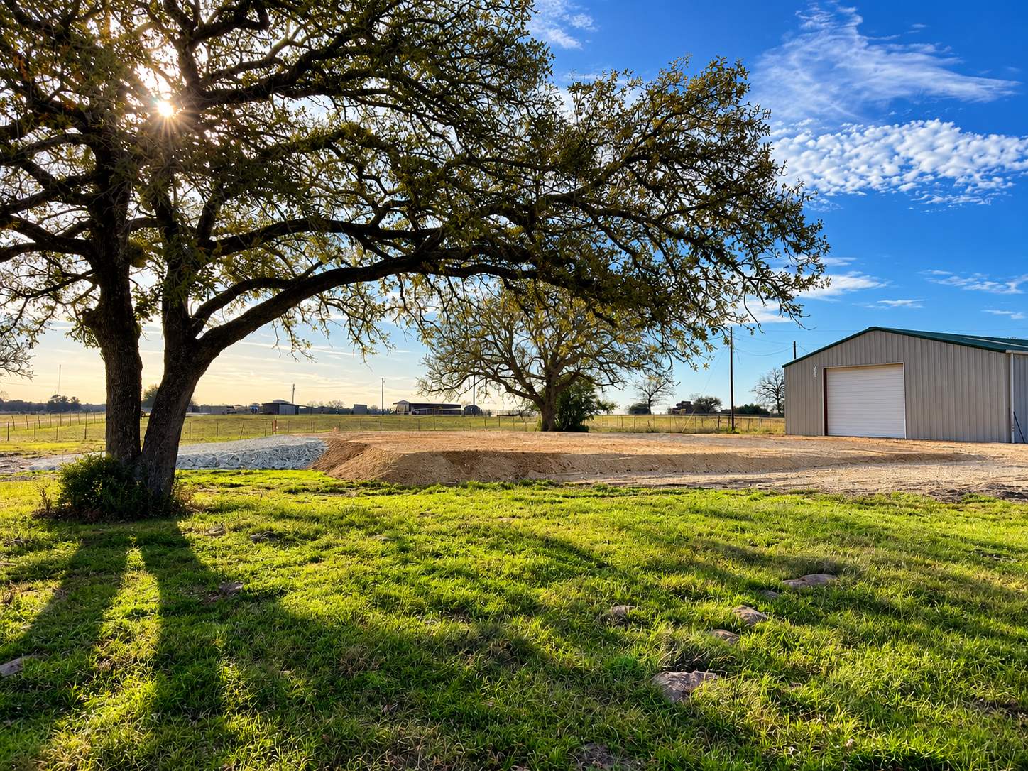 Finished base pad next to a metal building under a large oak tree