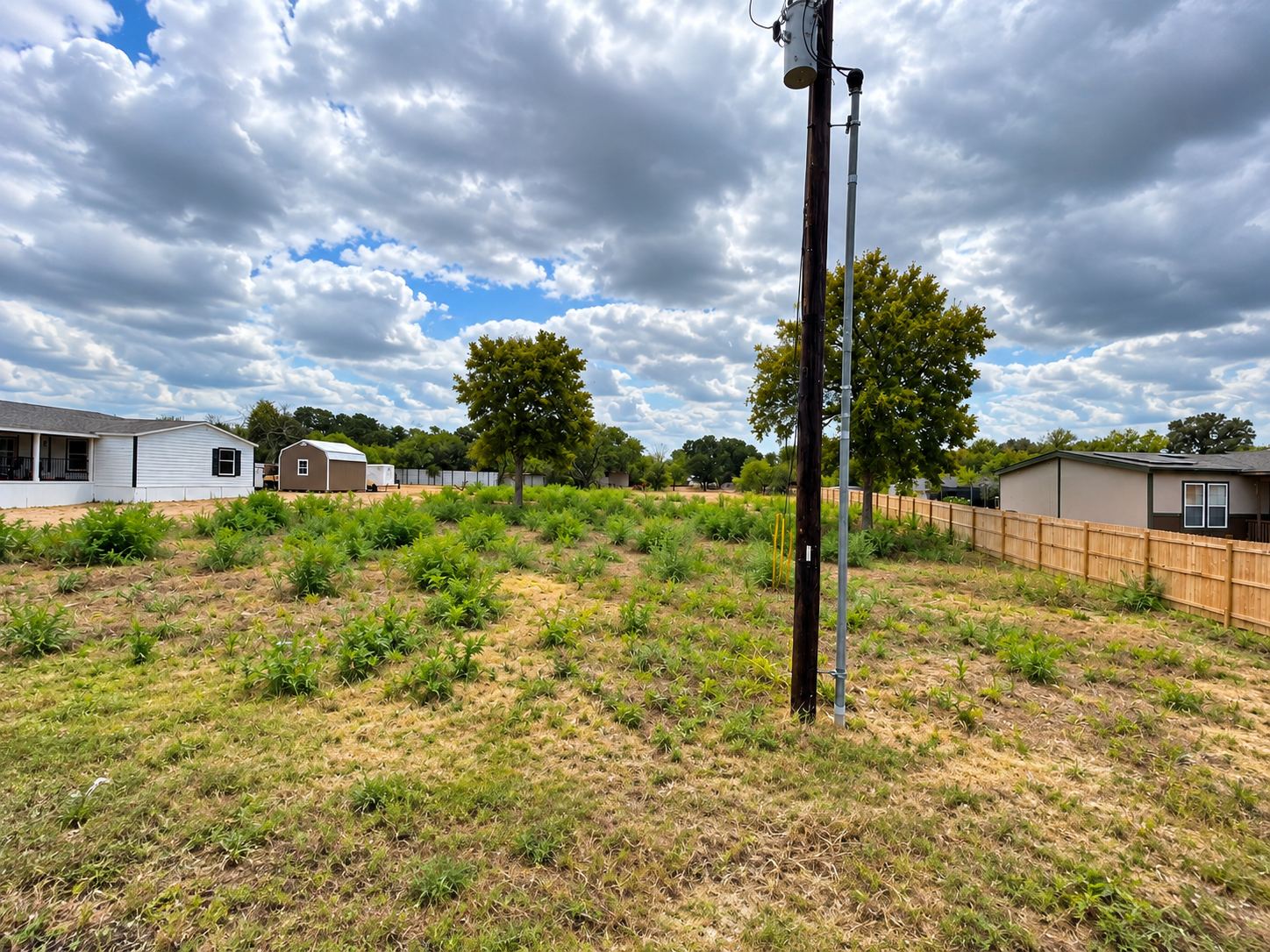 Lot covered in tall grass and weeds before land clearing, with a utility pole and fence