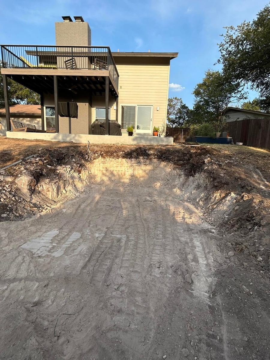 Excavated area behind a house with equipment tracks in the soil